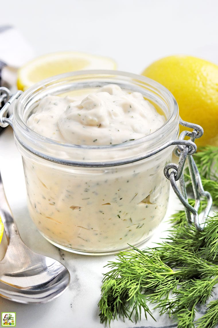 Closeup of a jar of tartar sauce with spoon, lemon, and fresh dill.