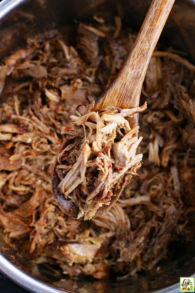A wooden spoon stirring shredded Instant Pot pork in an open pressure cooker.