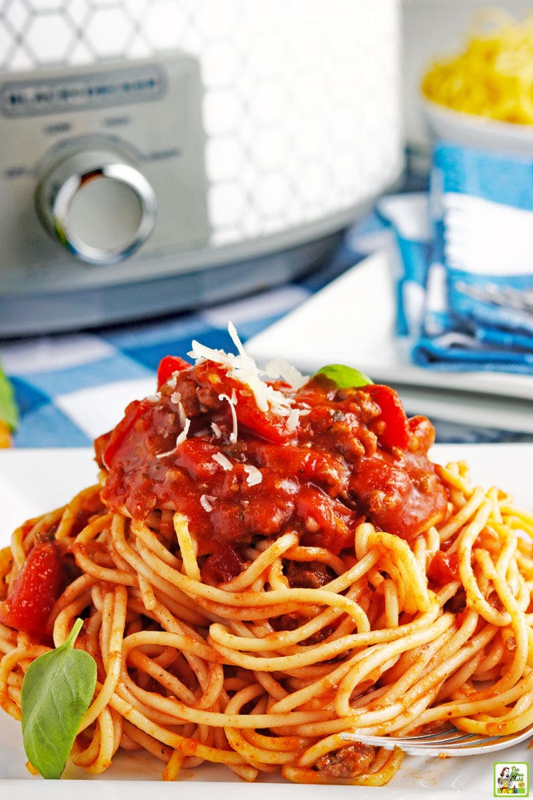 Closeup of a pile of slow cooker spaghetti sauce on pasta with a slow cooker and blue and white napkins in the background.
