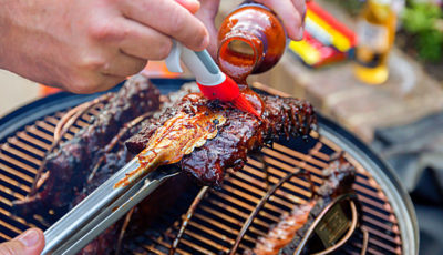 Brushing BBQ sauce on racks of pork ribs during grilling.