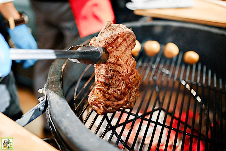 Flipping a grilled steak with tongs on a round ceramic smoker grill combo.