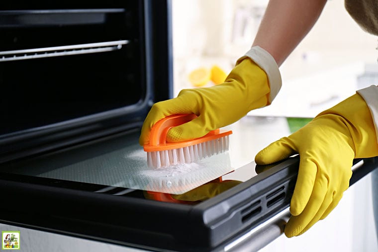 Woman wearing yellow rubber gloves cleaning oven with baking soda and scrub brush.