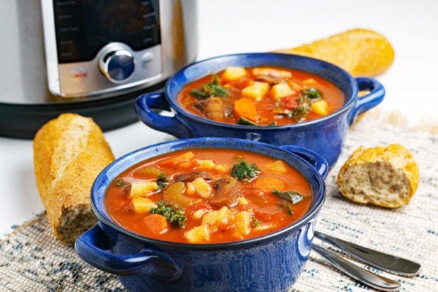 Two blue bowls of vegetable soup with bread, spoon, and an Instant Pot.