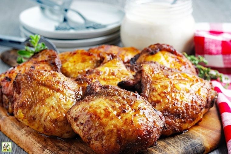 Καπνιστά μπούτια κοτόπουλου σε ξύλινο ξύλο κοπής με πιάτα, πιρούνια, σάλτσα και χαρτοπετσέτες.