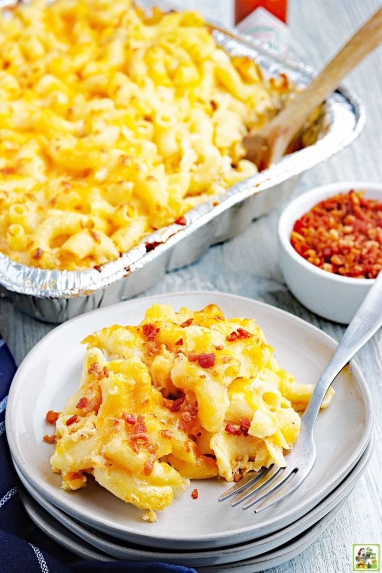 Ένα λευκό πιάτο με mac και τυρί, ένα δίσκο με μαγειρεμένα μακαρόνια και τυρί και ένα μικρό μπολ με θρυμματισμένο μπέικον.