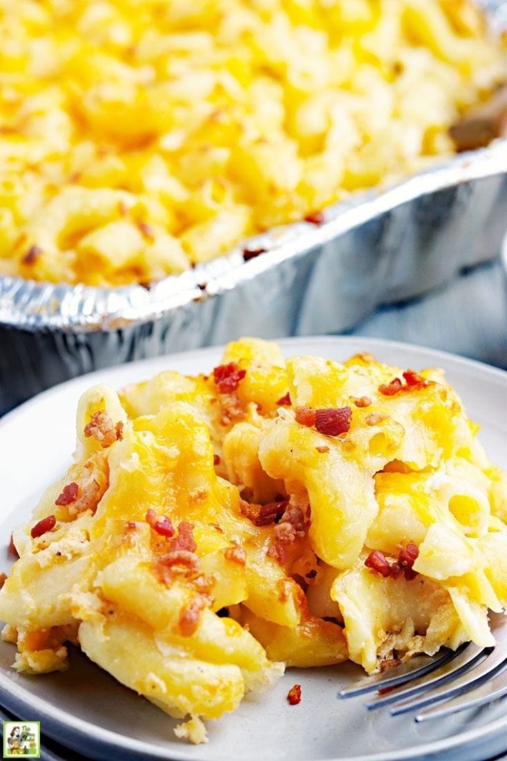 Closeup of mac and cheese with crumbled bacon on a white plate with fork and more in a casserole dish in the background.