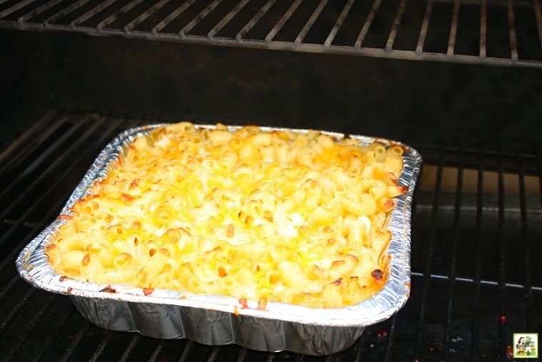 An aluminum baking dish of mac n cheese being cooked on a smoker grill.