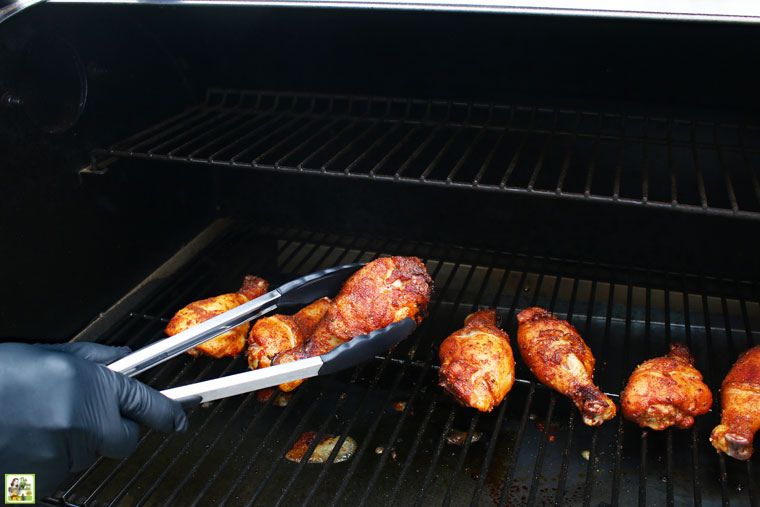 A gloved hand with tongs grilling up chicken legs.