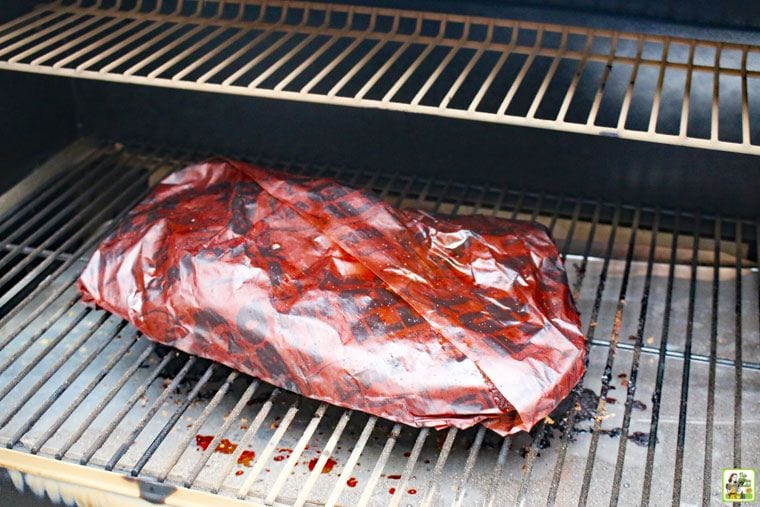 Wrapped smoked brisket cooking on a Traeger smoker grill.