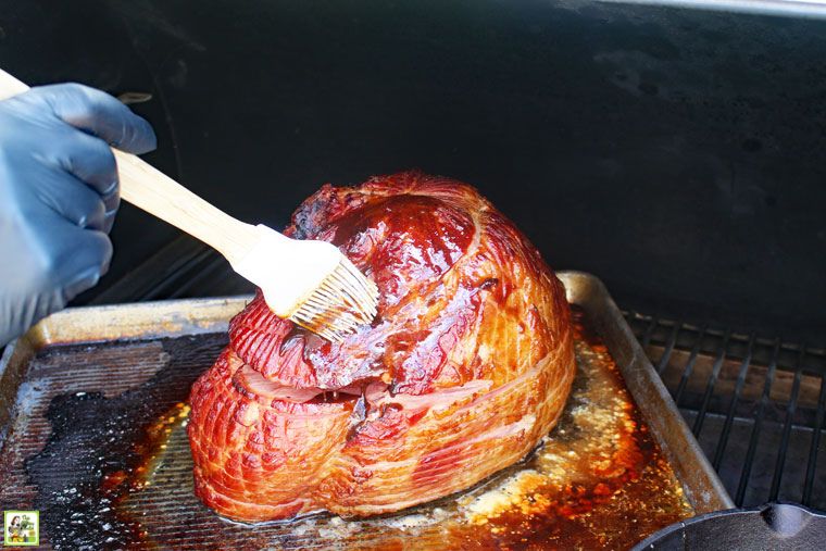 Using a basting brush to apply glaze to a spiral cut bone in ham on a pan placed inside a pellet smoker grill.