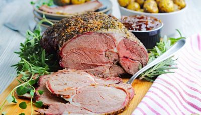 Sliced smoked leg of lamb on a wooden cutting board with sauce and sides.cutting board