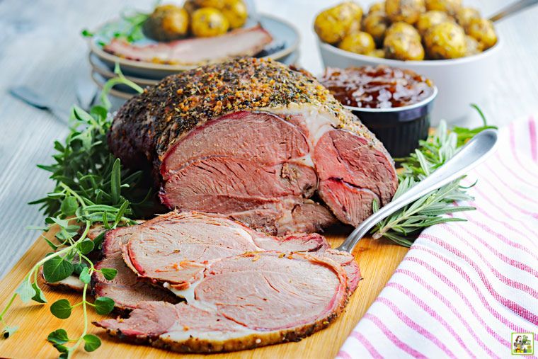 Sliced smoked leg of lamb on a wooden cutting board with sauce and sides.cutting board